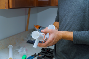 Fontanero sujetando tubería de plástico del fregadero de una cocina por la fuga de agua